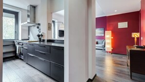 A modern kitchen with dark cabinetry, a stainless steel range hood, and a window providing natural light. - Music Bridge Apartment (Roma)