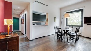 A modern kitchen with a built-in oven, a dining area with a round table and chairs, and a large window providing natural light. - Music Bridge Apartment (Roma)