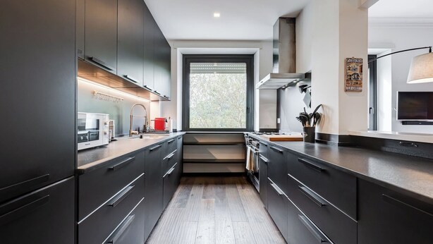 A modern kitchen with dark cabinetry, a central island, and a large window providing natural light. - Music Bridge Apartment (Roma)