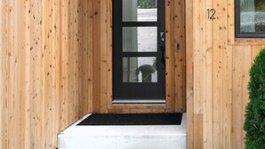 Eine Holzwand mit einer schwarz gerahmten Tür und einer kleinen Veranda.