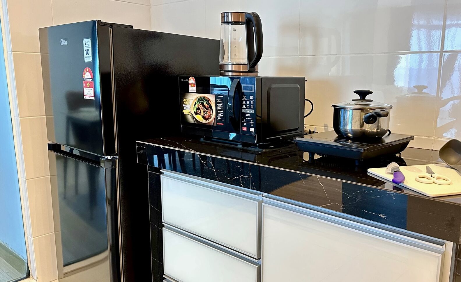 A modern kitchen with a black refrigerator, a coffee maker, a microwave, and a stove.