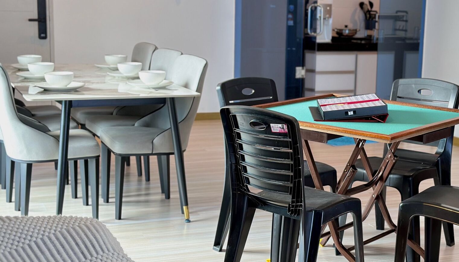 Un comedor moderno con una mesa preparada para cuatro personas, sillas negras y un mantel verde azulado.