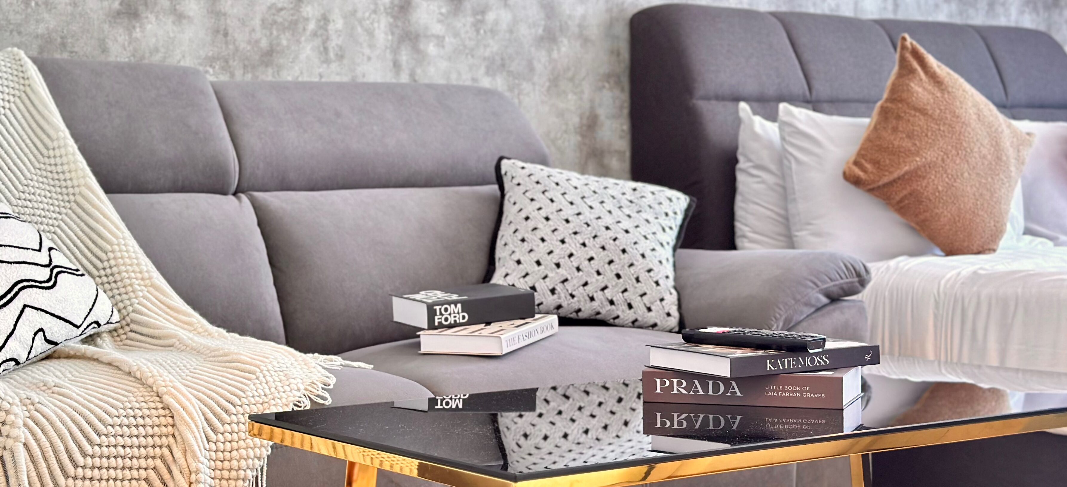 Una sala de estar con un sofá gris, una mesa de centro y una cama con almohadas.