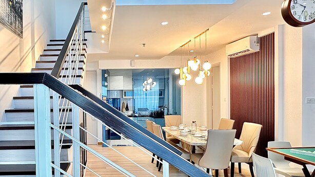 Un intérieur moderne avec un escalier, un coin repas et une horloge au mur.