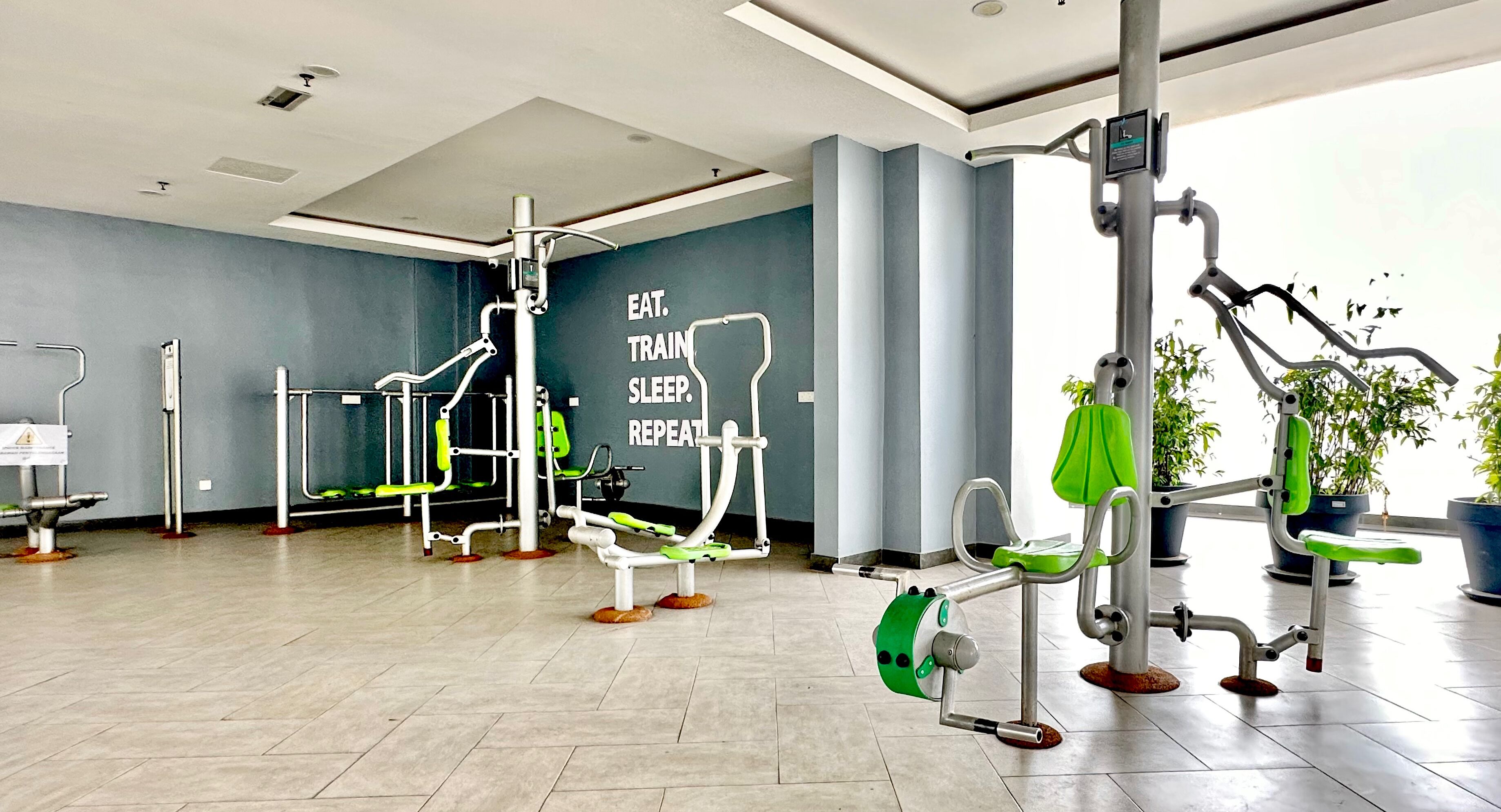 A modern gym with various exercise equipment, a motivational quote on the wall, and potted plants.