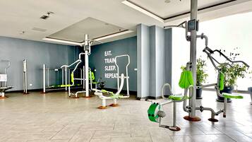 A modern gym with various exercise equipment, a motivational quote on the wall, and potted plants.
