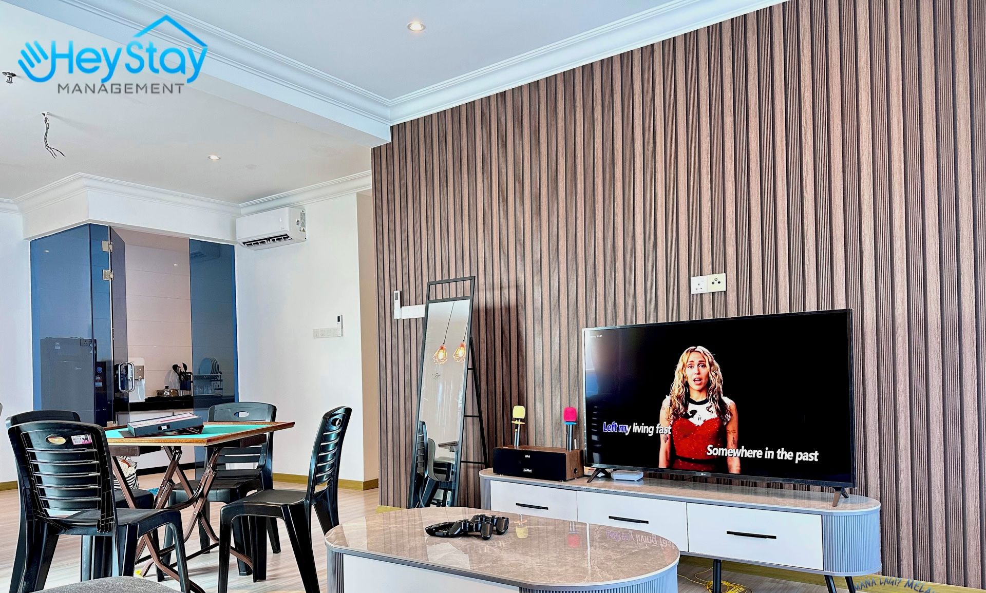 A modern living room with a flat-screen TV, a dining area with chairs, a sofa, and a wooden accent wall.