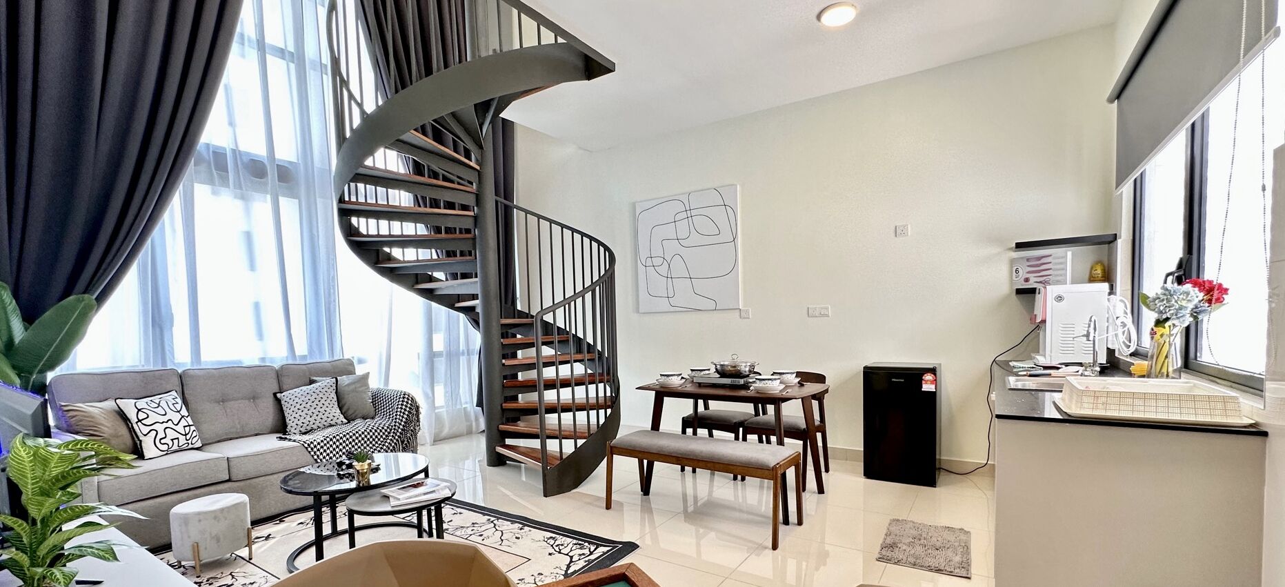 A modern living room with a spiral staircase, a dining area, and a kitchenette.