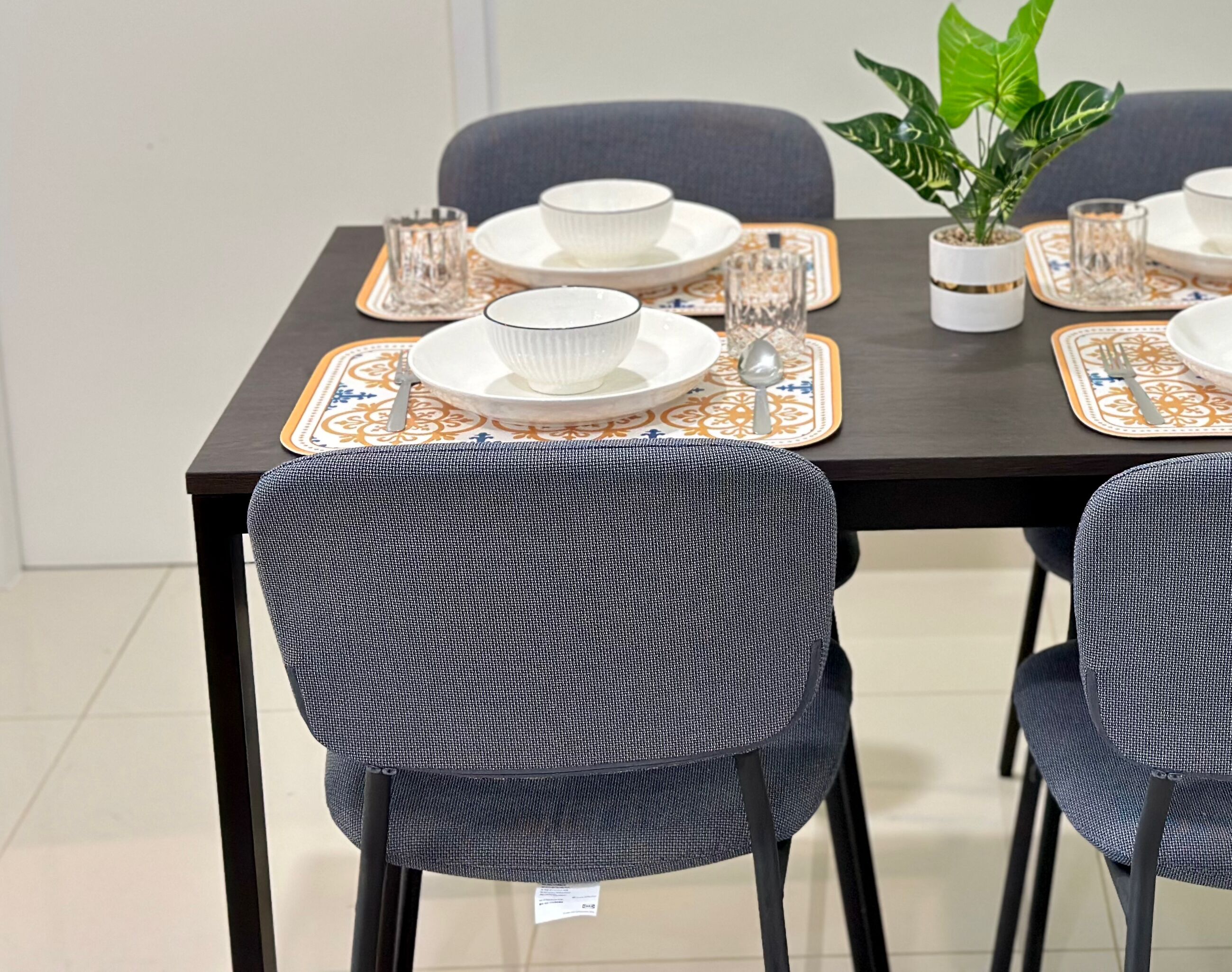 A dining table set with plates, bowls, glasses, and a potted plant.