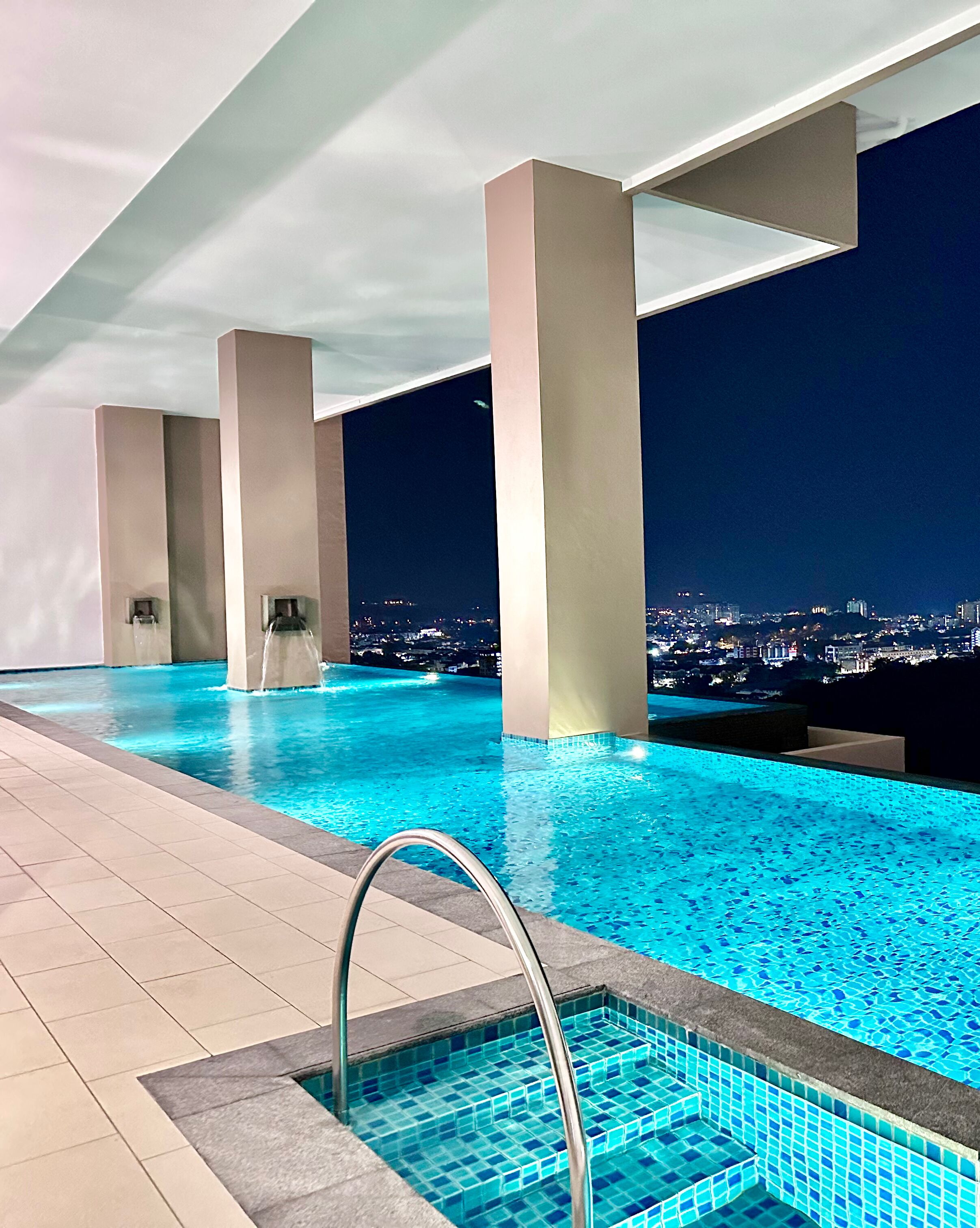 An indoor infinity pool with a city view at night.