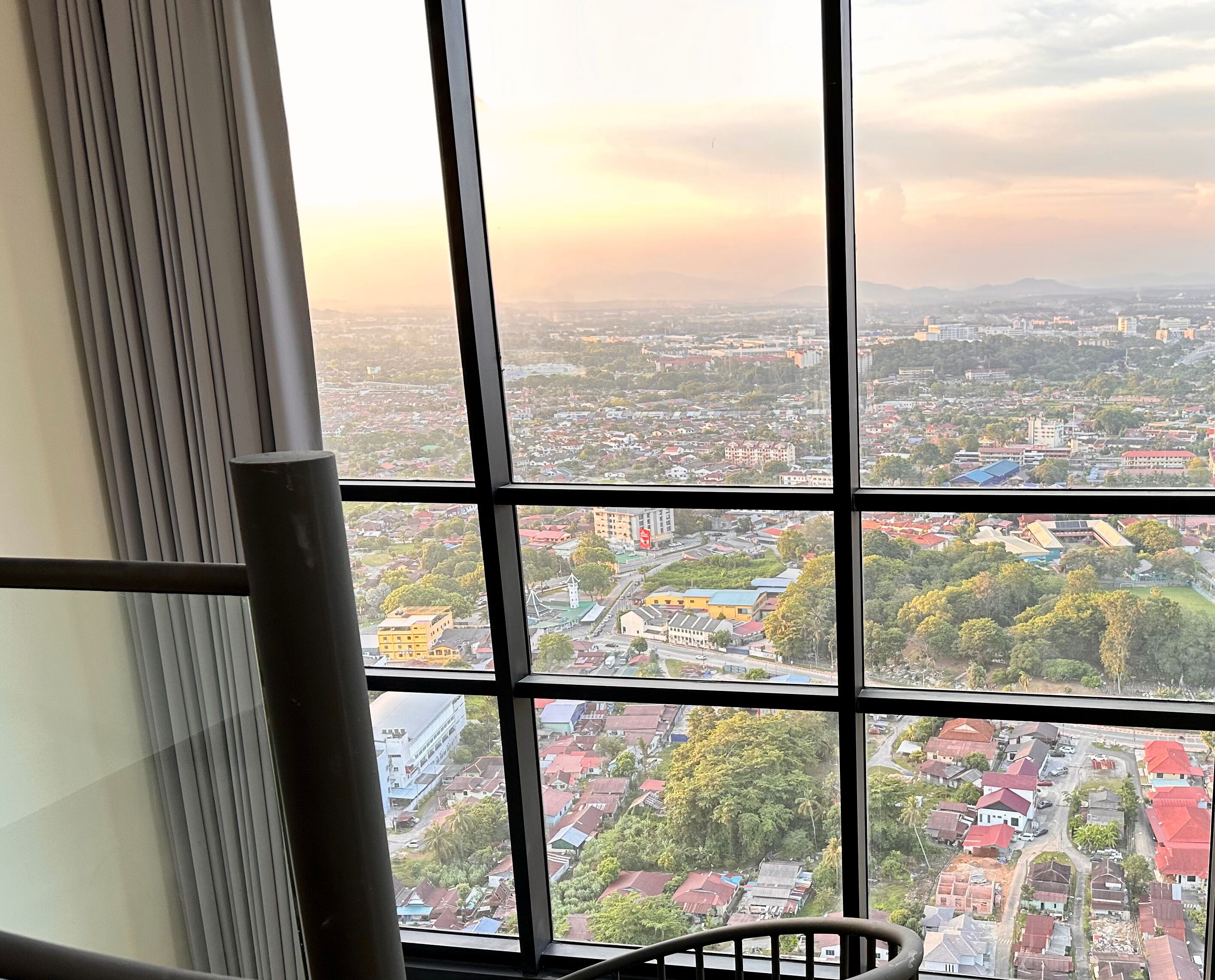 A view from a window with multiple panes, overlooking a cityscape with various buildings and greenery.