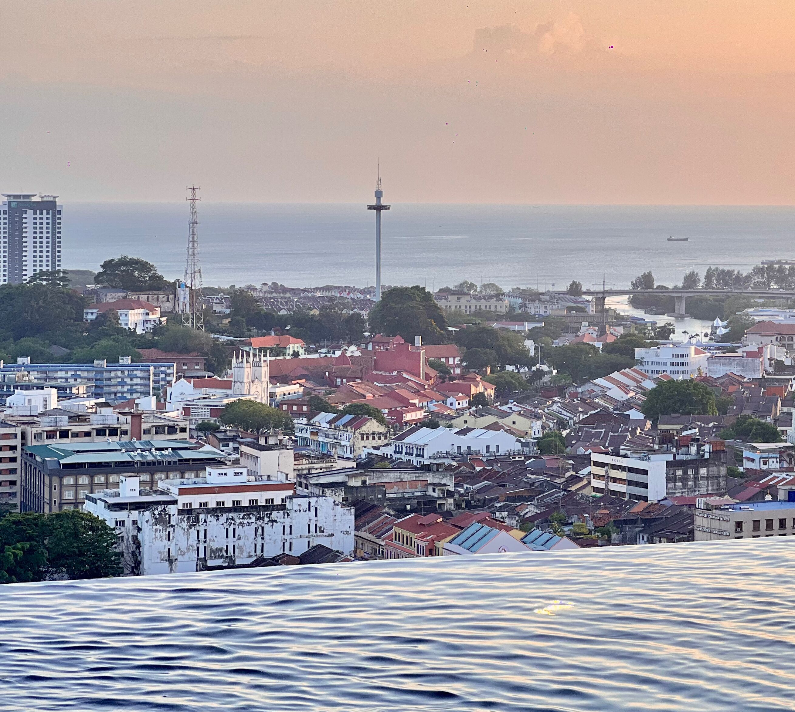 A coastal cityscape with a prominent tower, dense residential buildings, and a body of water in the foreground.