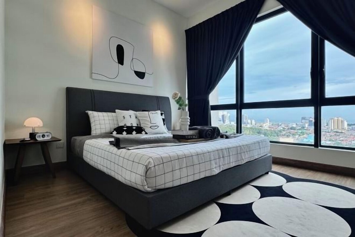 A modern bedroom with a large bed, a nightstand, a radio, and a view of the city through large windows.
