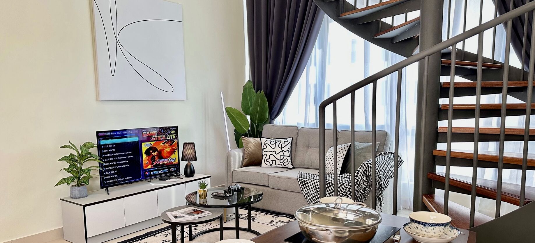 A modern living room with a sofa, coffee table, and TV. There's a staircase with wooden railings and a potted plant.