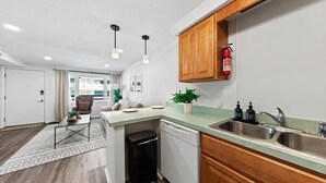 Cocina compacta con lavavajillas, un lavabo, armarios de madera y un extintor.