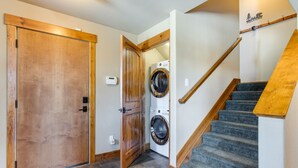 Een wasruimte met een wasmachine en droger, een houten deur en een trap met houten leuning.
