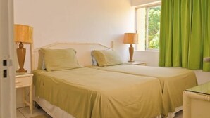 A double room with two beds, a window with green curtains, and bedside lamps. - Beach Ready Condo than 5 mins. away from your private beach and Margaritaville. (Ocho Rios)