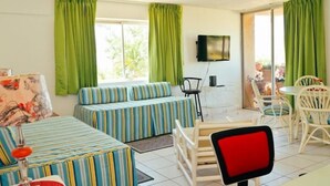 A room with a sofa set, a dining table with chairs, a TV mounted on the wall, and large windows with curtains. - Beach Ready Condo than 5 mins. away from your private beach and Margaritaville. (Ocho Rios)