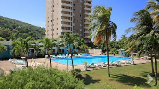 A hotel with a swimming pool surrounded by palm trees and lounge chairs. - Beach Ready Condo than 5 mins. away from your private beach and Margaritaville. (Ocho Rios)
