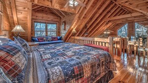 Un dormitorio de cabaña de madera con una cama grande, un ventilador de techo y vistas al exterior a través de las ventanas.