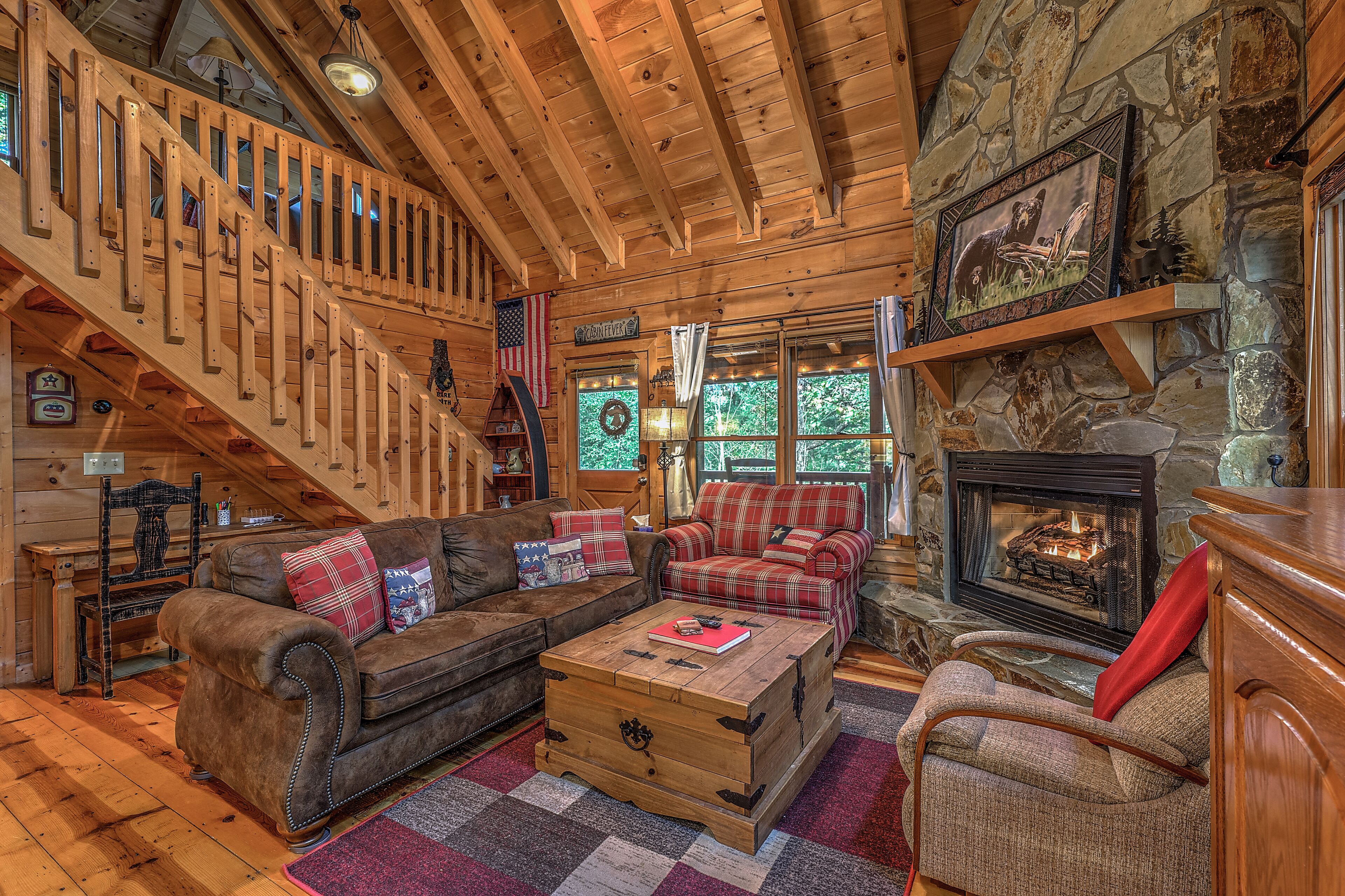 A log cabin interior with a fireplace, wooden staircase, and a cozy seating area.