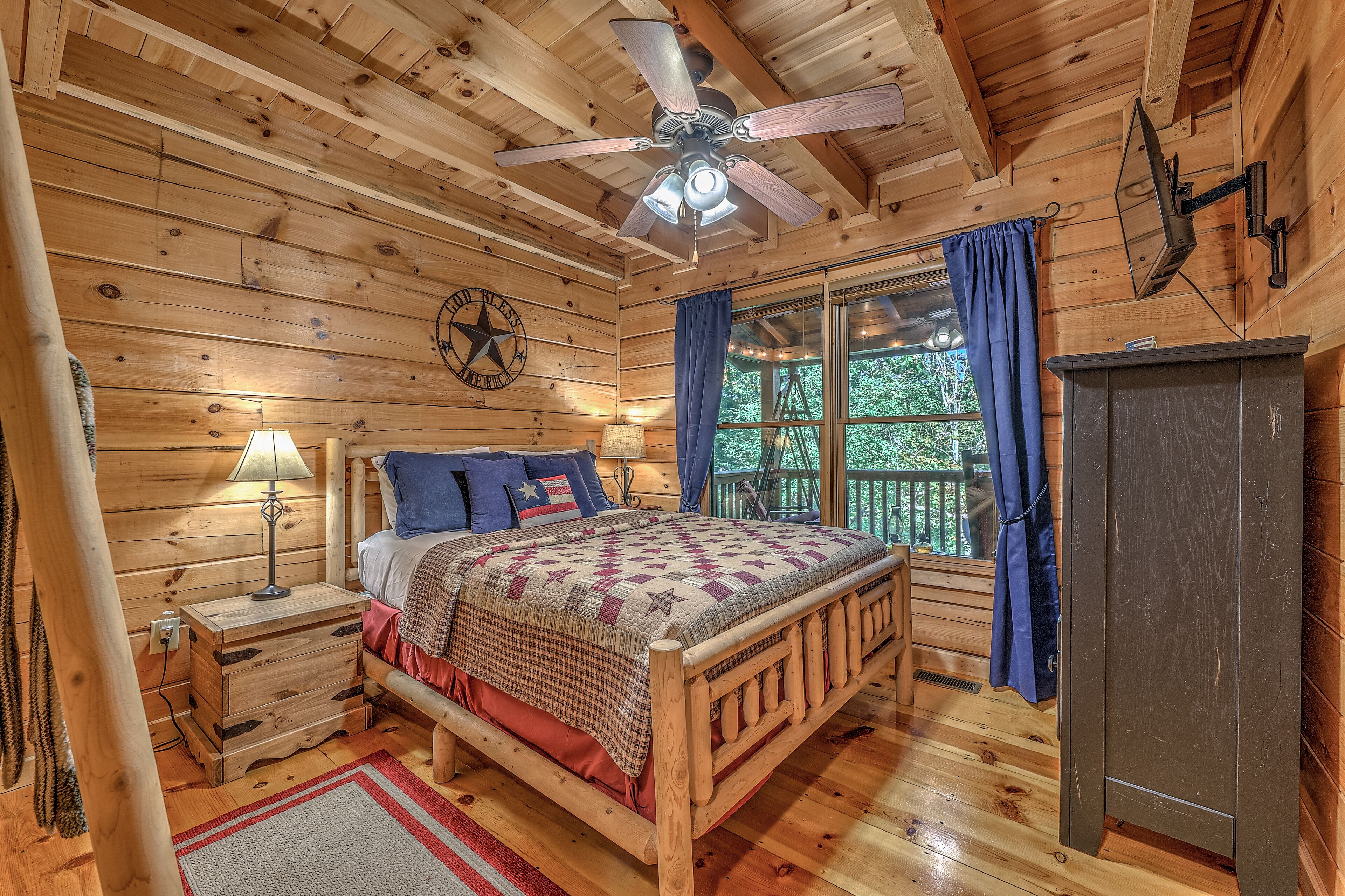 Een slaapkamer in een houten hut met een bed, nachtkastje, lamp en plafondventilator.