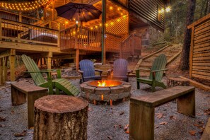 Um deck de madeira com cadeiras Adirondack, uma lareira e uma área coberta com luzes de corda.