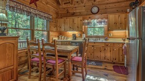 Cocina de cabaña de madera con una mesa de comedor, sillas, un refrigerador y un reloj en la pared.