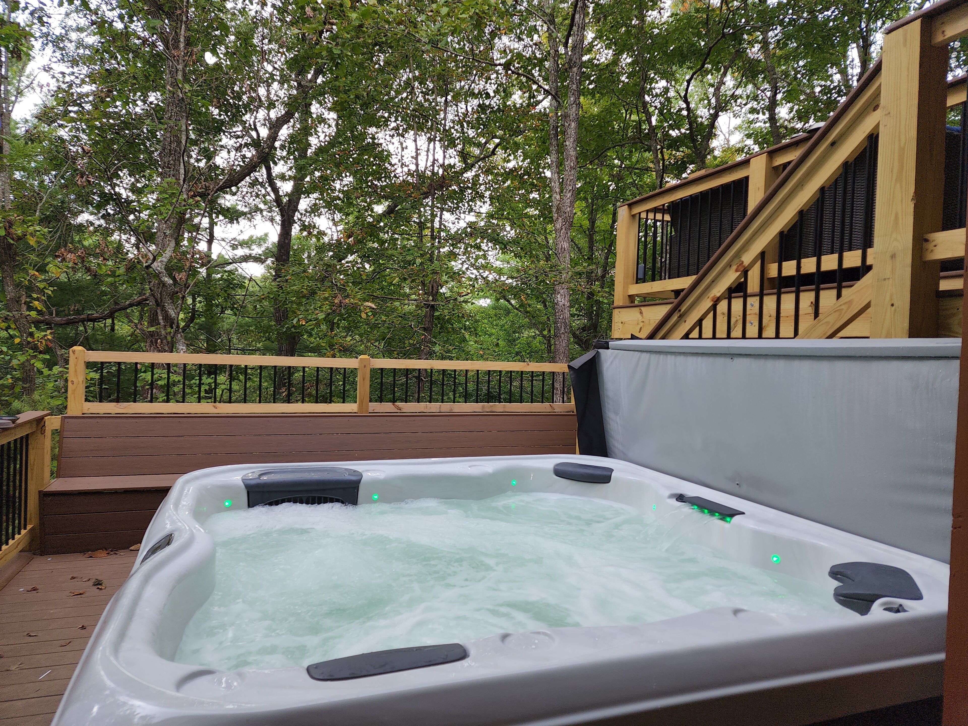 Een hottub op een houten terras met een reling en bomen op de achtergrond.