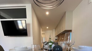 Un comedor moderno con una mesa de madera dispuesta para cuatro comensales, un televisor de pantalla plana en la pared y una cocina al fondo.
