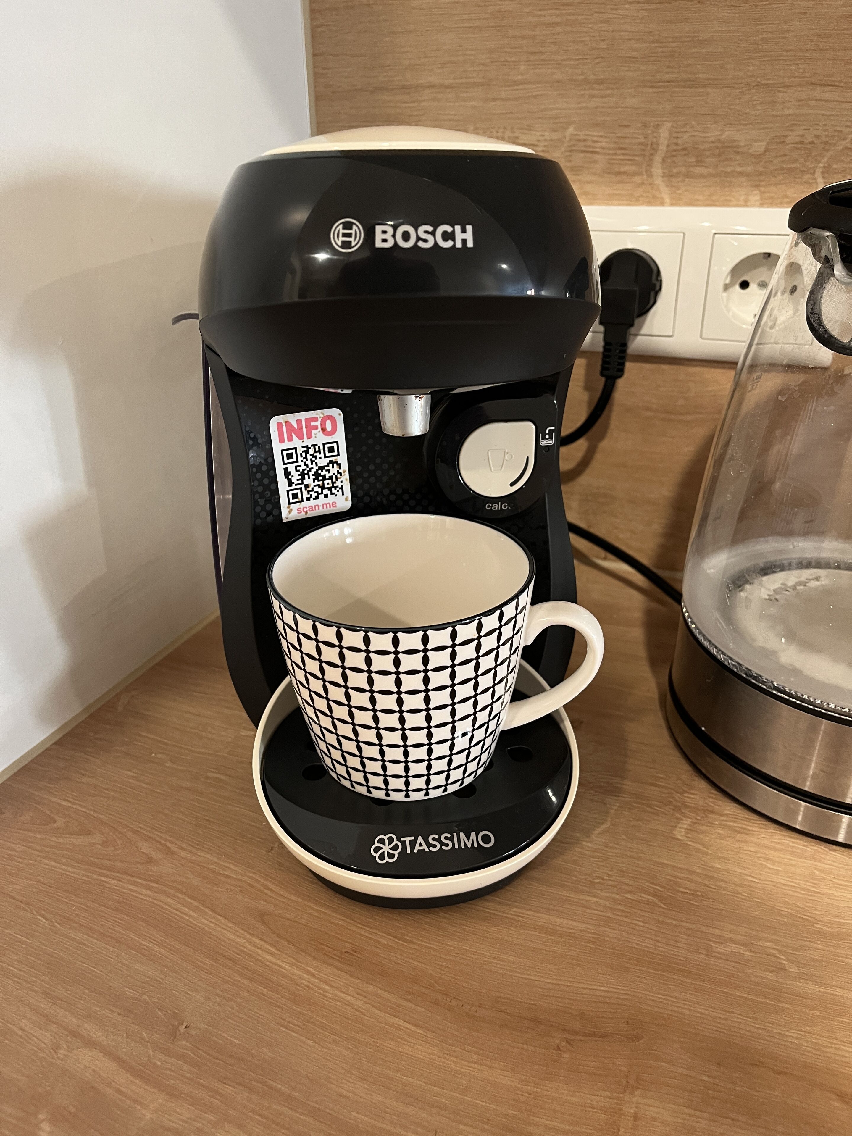 En kaffebryggare med en kopp på ett litet fat.