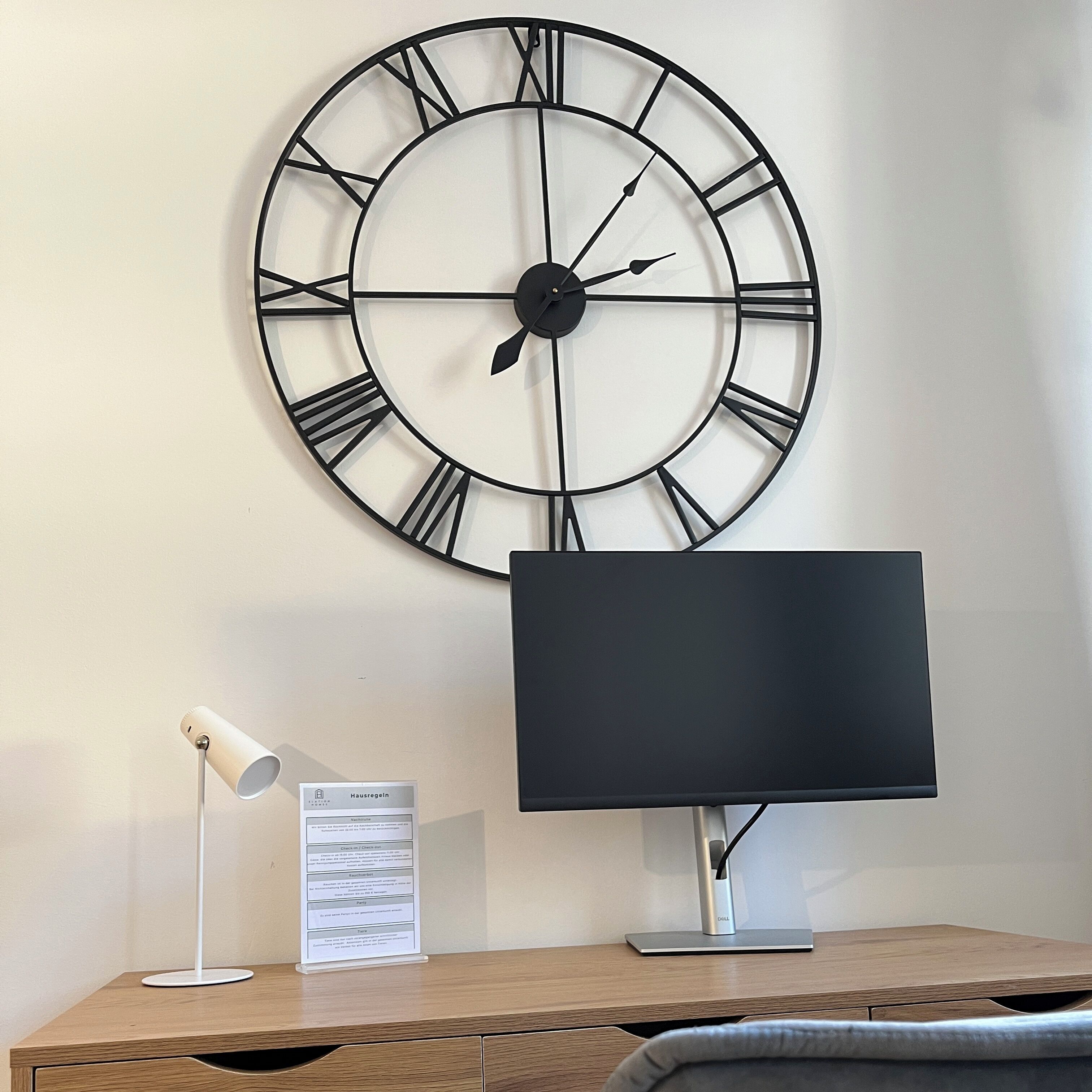 A desk with a monitor, a lamp, and a wall clock.