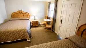 A bedroom with two beds, a wooden headboard, a bedside table with a lamp, a small round table, and a chair. - Country Inn & Cottages (Fredericksburg)