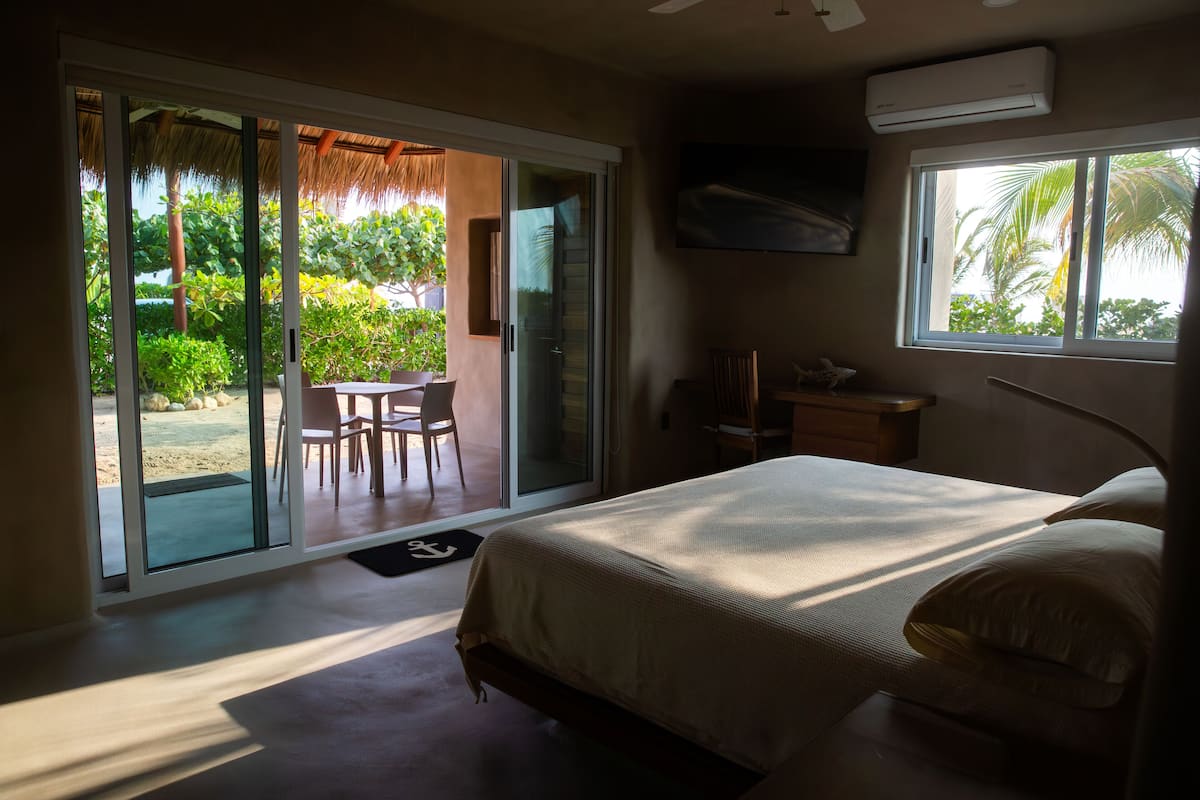 Ein Schlafzimmer mit Bett, Schreibtisch, Stuhl und Blick auf eine Terrasse mit Tisch und Stühlen.