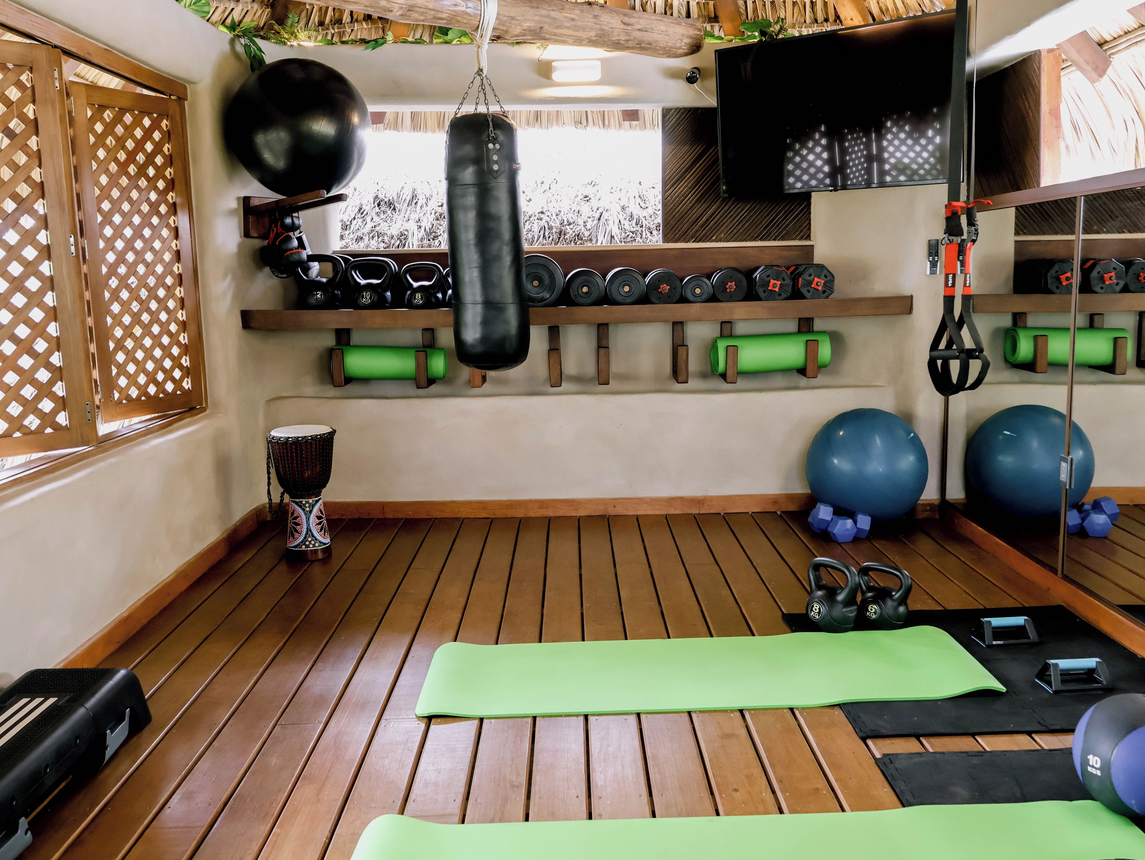 A gym with wooden flooring, exercise mats, kettlebells, dumbbells, a punching bag, and a yoga ball.