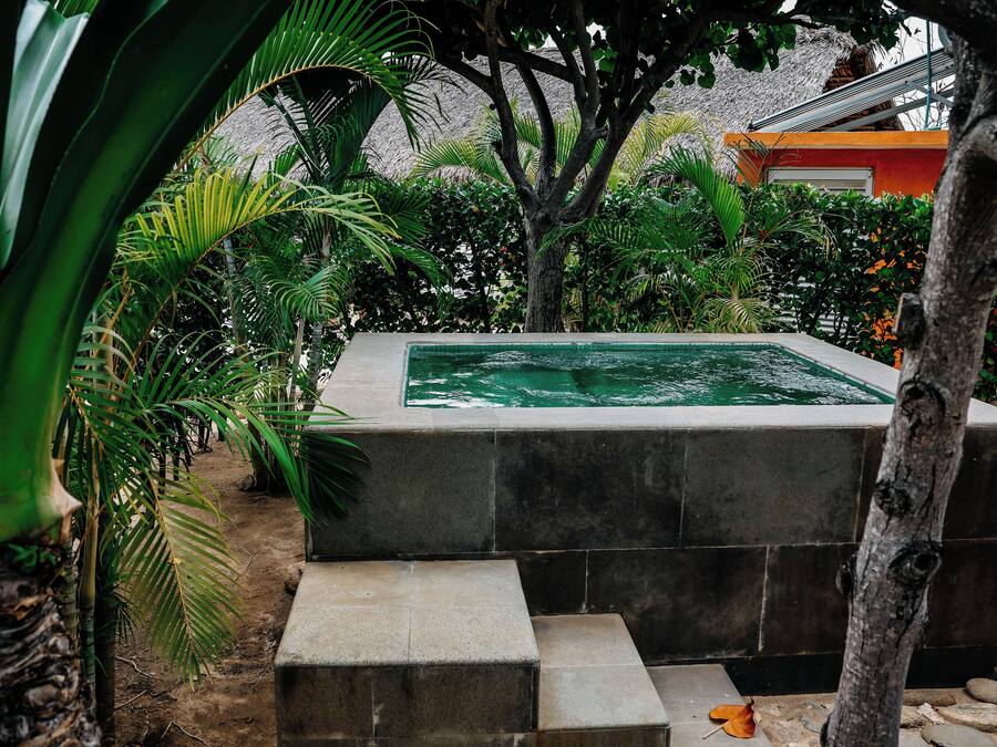A swimming pool surrounded by lush greenery, with a stone structure and steps leading down to the water.