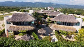 A resort with thatched-roof huts, a pool, and a view of distant mountains. - El Origen Villas & Spa Puerto Escondido (San Pedro Mixtepec)