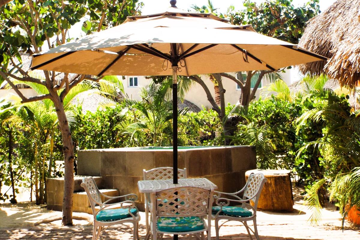 Eine Terrasse im Freien mit Tisch und Stühlen, einem großen Sonnenschirm und üppiger Bepflanzung.