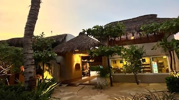 A resort with thatched-roof buildings, palm trees, and a paved walkway.