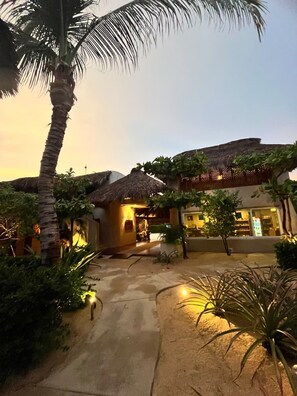 A resort with thatched-roof buildings, palm trees, and a paved walkway. - El Origen Villas & Spa Puerto Escondido (San Pedro Mixtepec)