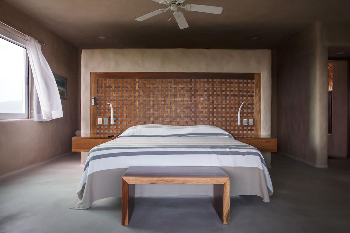 Ein modernes Schlafzimmer mit einem großen Bett, einem Holzkopfteil, einem Nachttisch und einem Deckenventilator.