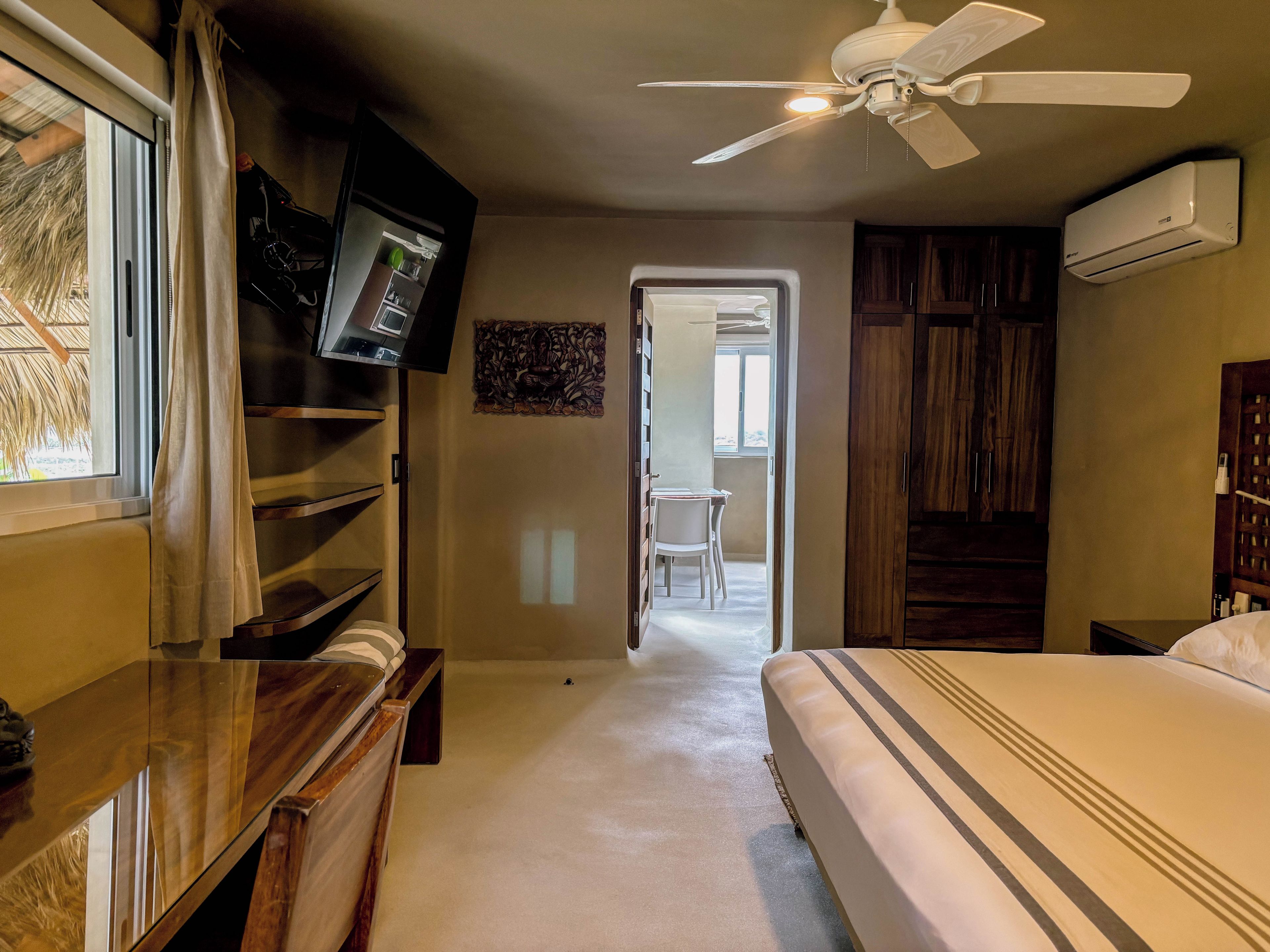 A hotel room with a bed, a TV mounted on the wall, a ceiling fan, and an air conditioning unit.