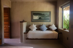 Un dormitorio con cama, mesita de noche, ventana con vista a palmeras y un cuadro de olas en la pared.