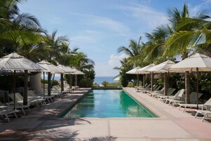 Ein Poolbereich mit Liegestühlen und Sonnenschirmen, umgeben von Palmen, mit Blick auf das Meer.