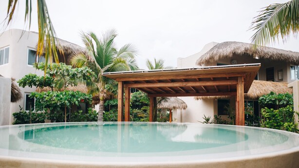 A circular pool with a wooden pergola in the center, surrounded by lush greenery and thatched-roof buildings. - El Origen Villas & Spa Puerto Escondido (San Pedro Mixtepec)