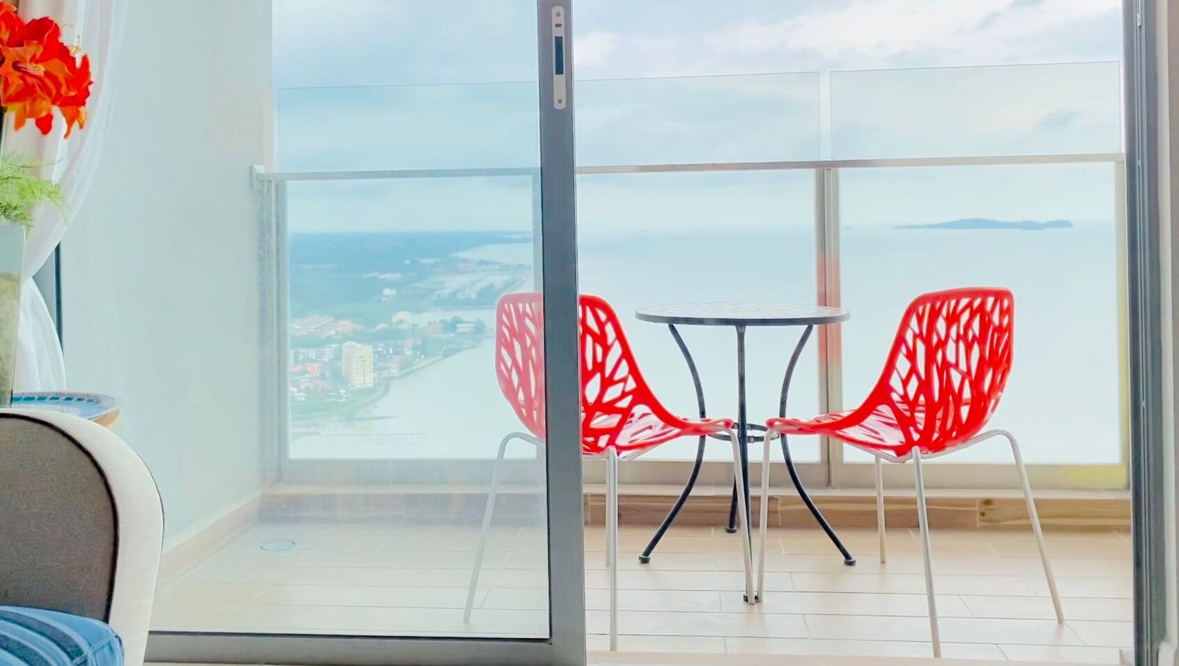 A balcony with a table and two chairs, overlooking a body of water and distant buildings.
