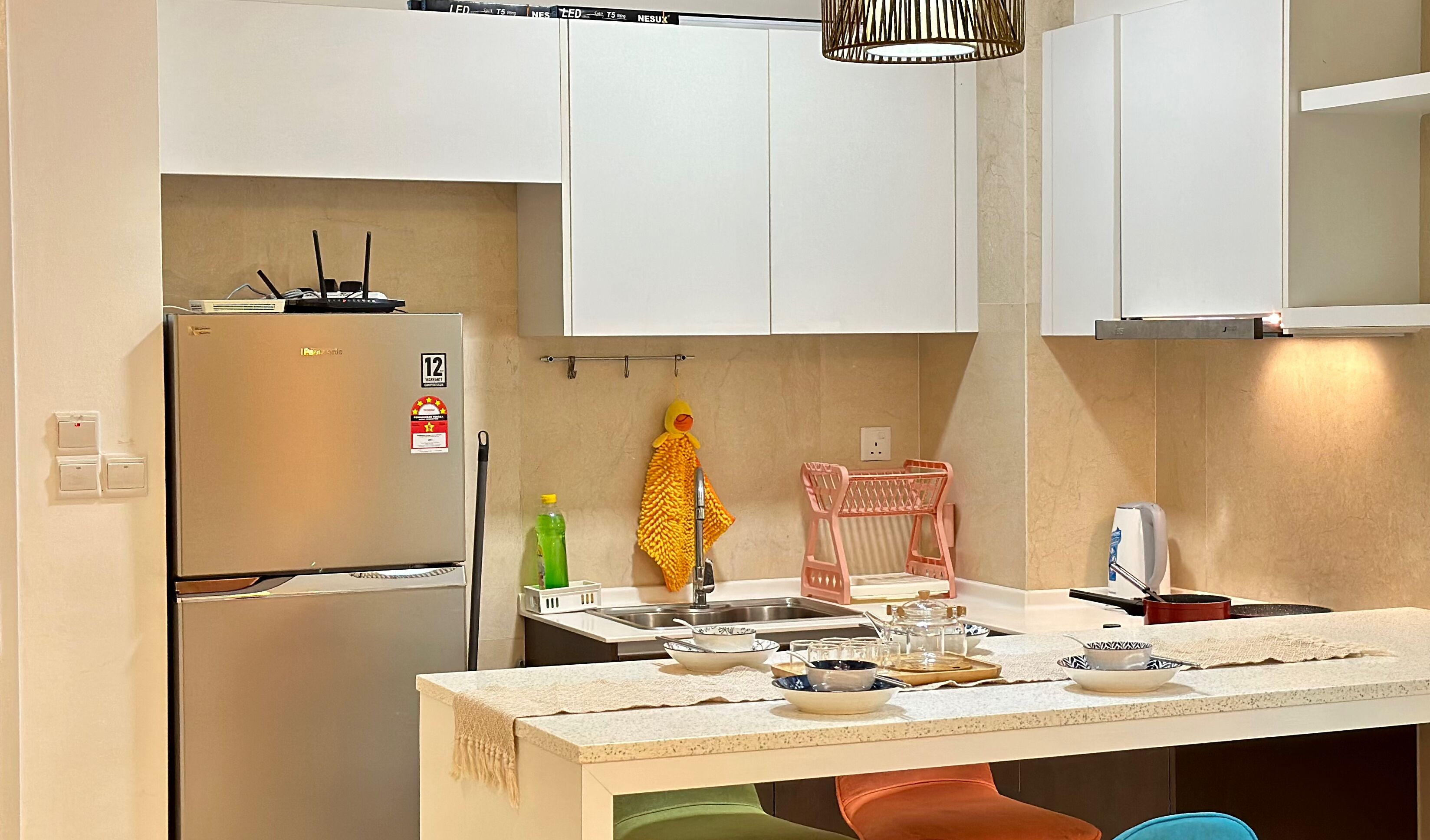 A modern kitchen with white cabinets, a stainless steel refrigerator, a sink, and a countertop with various kitchen items.
