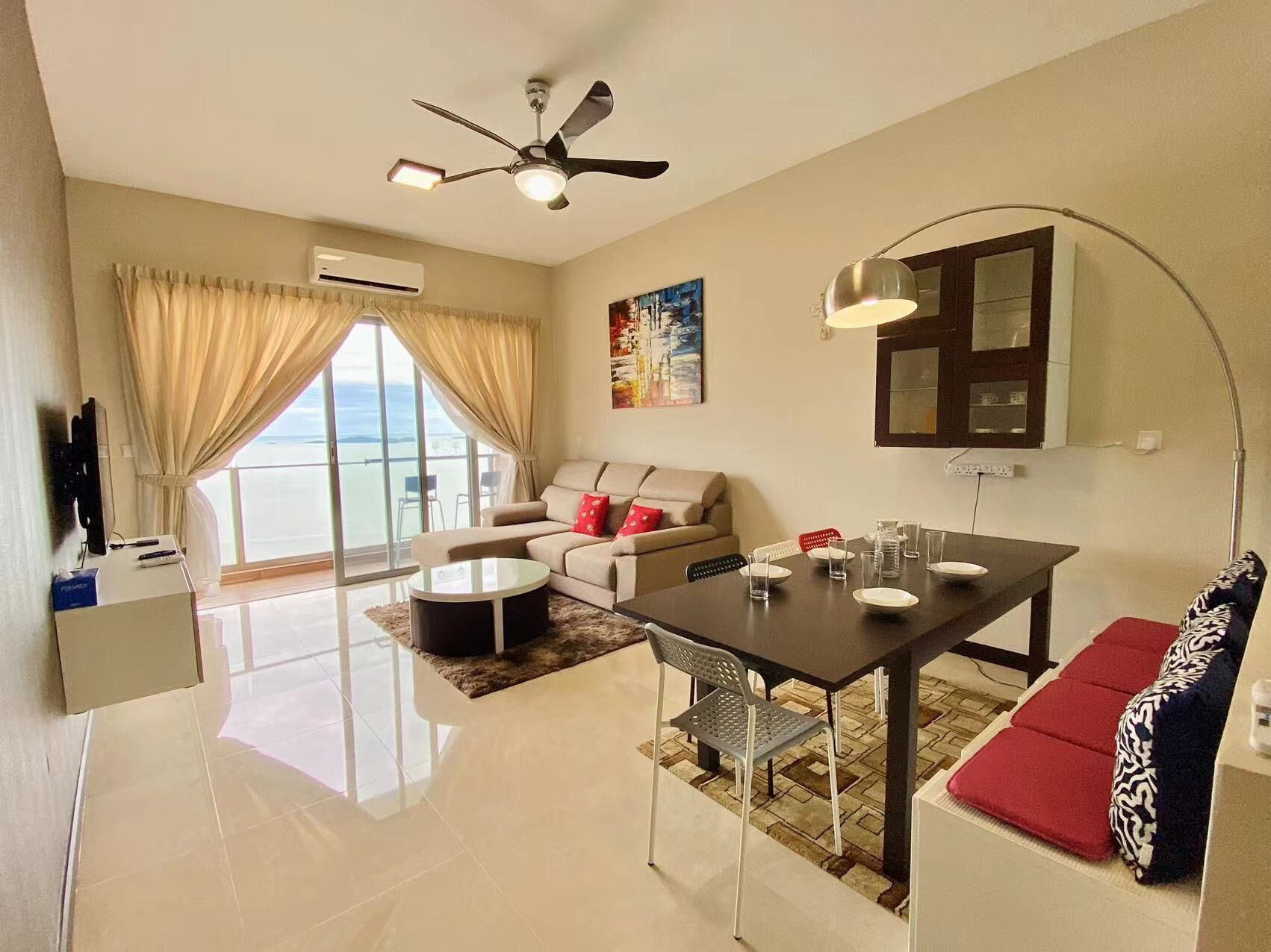 A modern living room with a sofa, a dining table, a ceiling fan, and a large window with curtains.