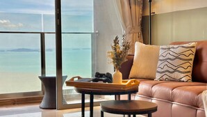 Un soggiorno moderno con un divano in pelle, un tavolino rotondo e un vaso con fiori secchi. Un'ampia finestra si affaccia sul mare e su isole in lontananza.
