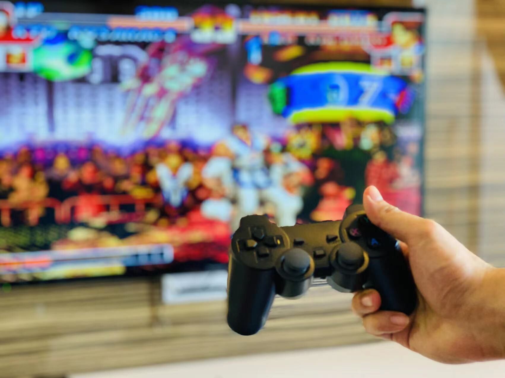 A hand holding a video game controller in front of a television displaying a colorful video game scene.